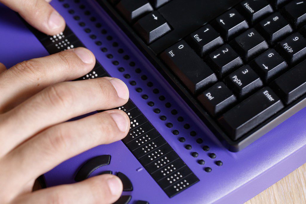 Hand using a braille keyboard for information and communication technology accessibility